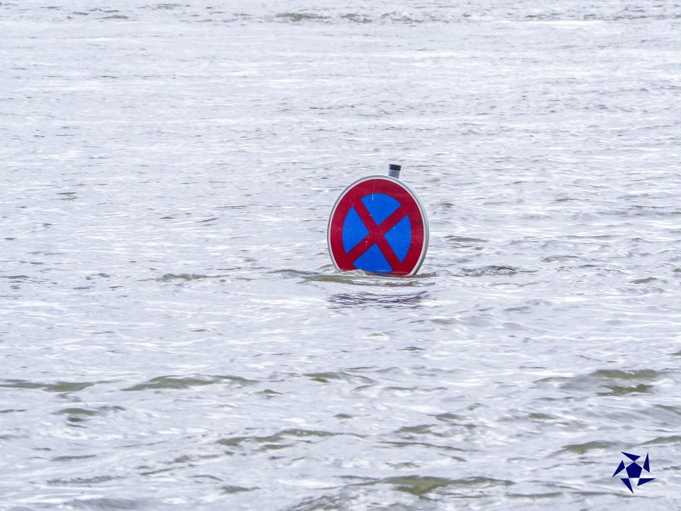 A "stop and parking forbidden" sign in the middle of an open field covered by fast flowing water