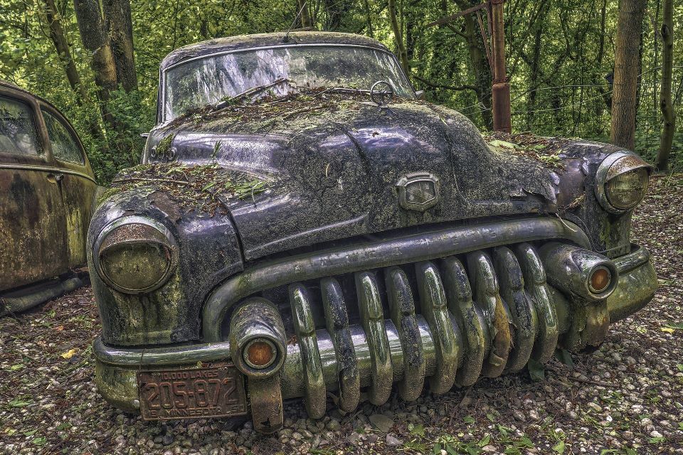 An abandoned vintage car that has a huge radiator that looks like a mouth full of teeth