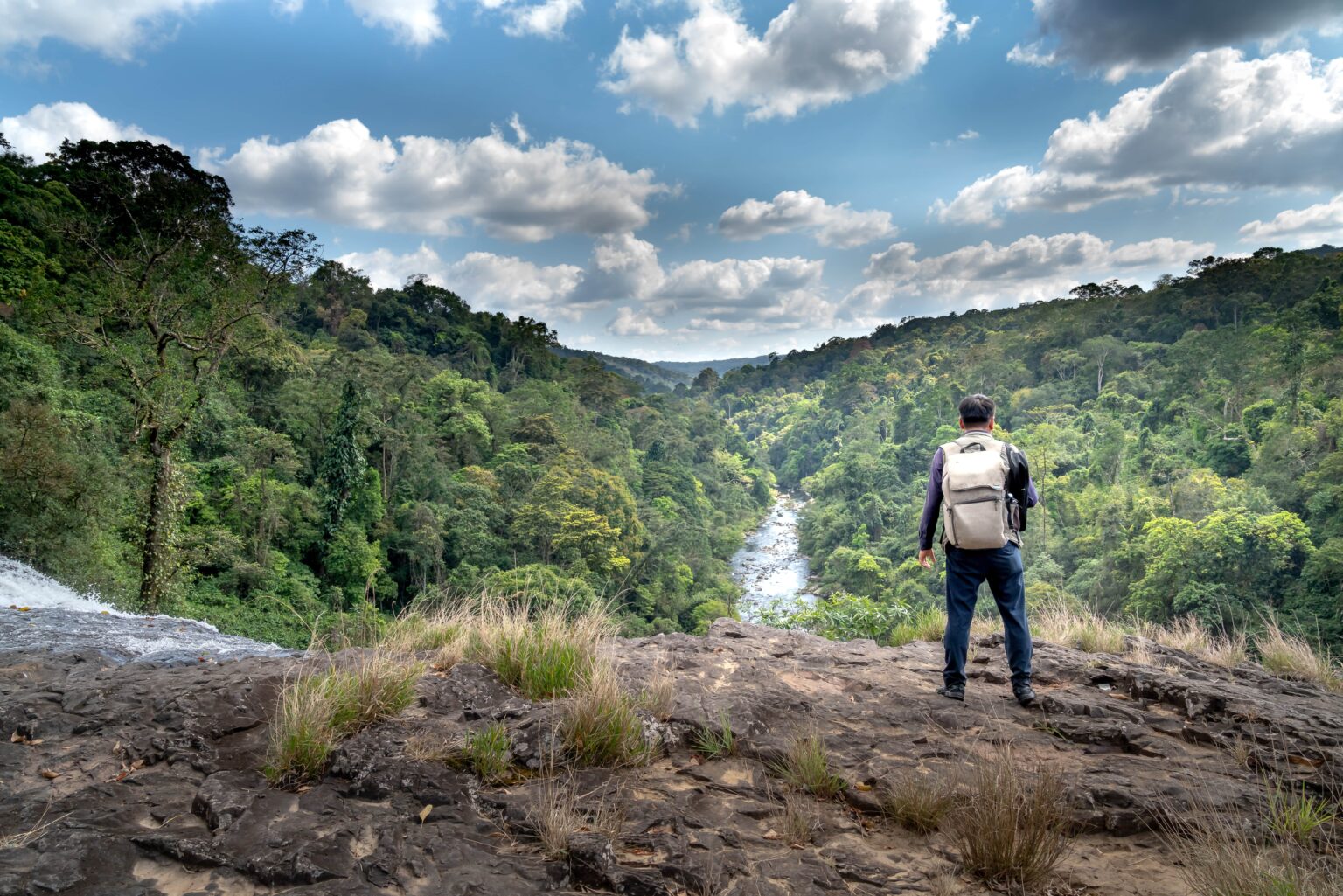 Uno de nuestros guías expertos, que está de pie en la cresta de una montaña con vistas a un río que fluye a través de una selva tropical, que te llevará al éxito financiero