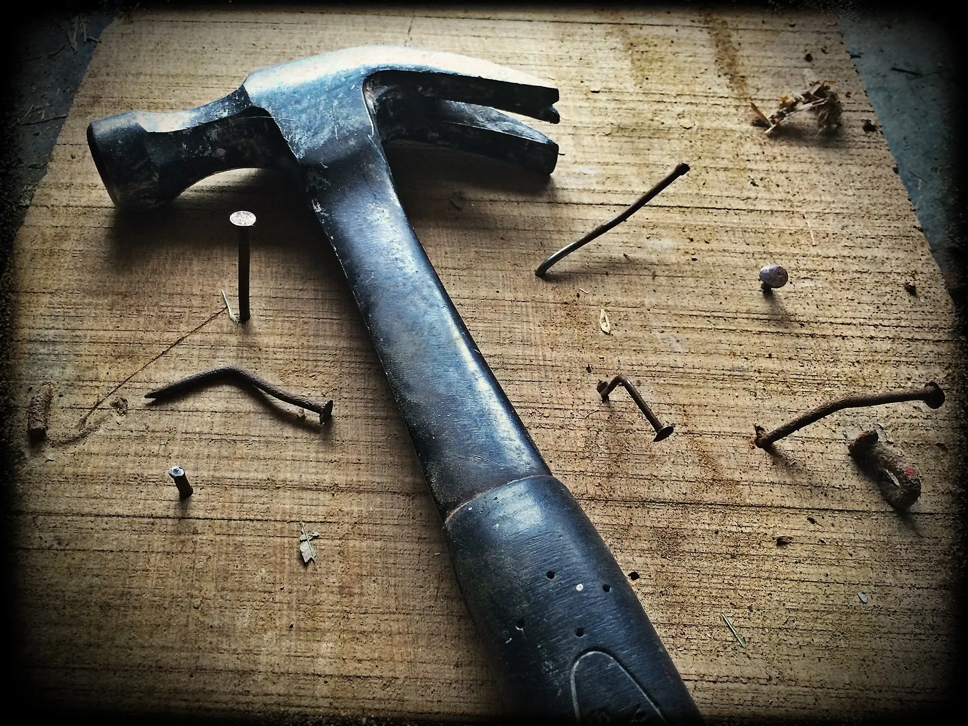 A black hammer on top of a block of wood into which many bent nails have been hammered